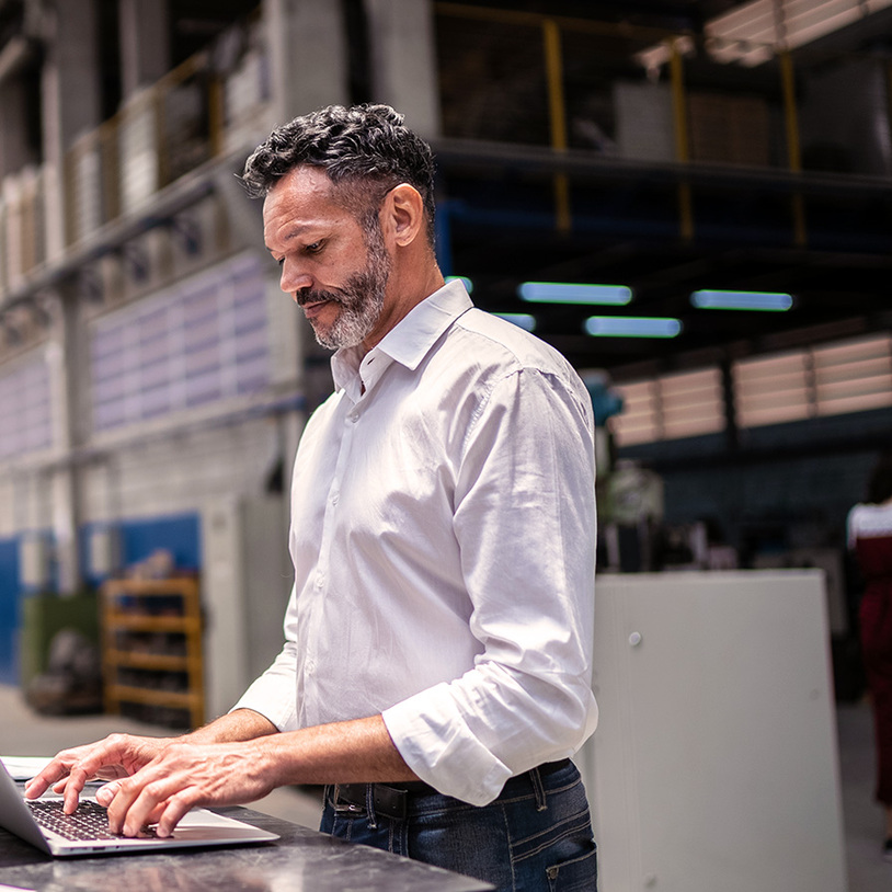 Mann in einer Lagerhalle tippt in Laptop