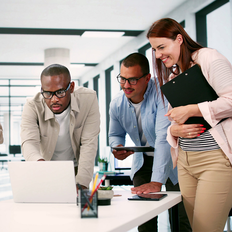 Drei Personen stehen am Schreibtisch und schauen auf einen Laptop