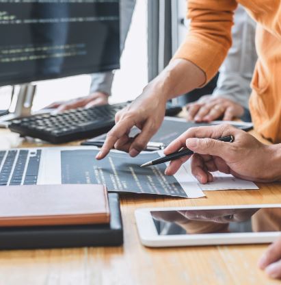 Foto von einem Schreibtisch mit Computer-Bildschirm, Tablet und Personen 